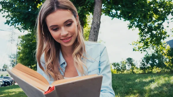 Jovem estudante alegre leitura livro no parque — Fotografia de Stock