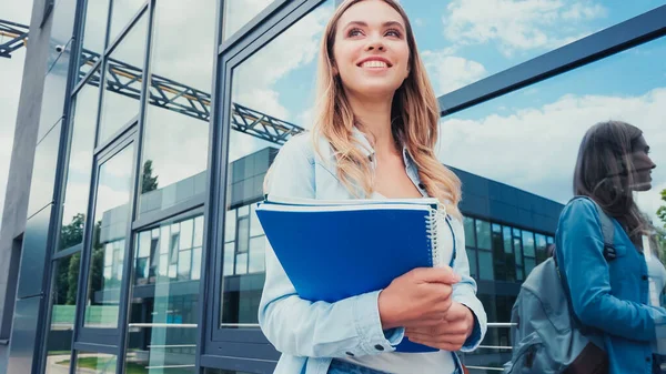 Joyful young student holding notebooks near building — Stock Photo