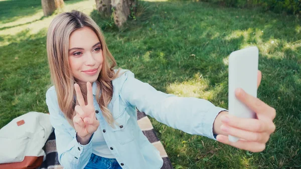 Sourire étudiant geste tout en prenant selfie dans le parc — Photo de stock