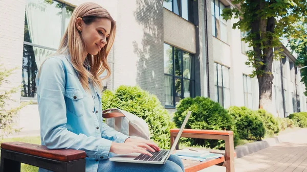 Étudiant joyeux en utilisant un ordinateur portable tout en étant assis sur le banc — Photo de stock