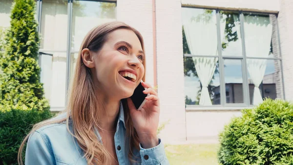 Fröhlicher Student spricht auf Smartphone in der Nähe von Gebäuden im Freien — Stockfoto