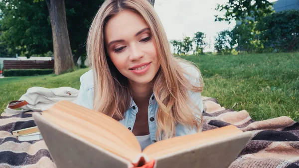 Молодой и улыбчивый студент читает книгу в парке — стоковое фото