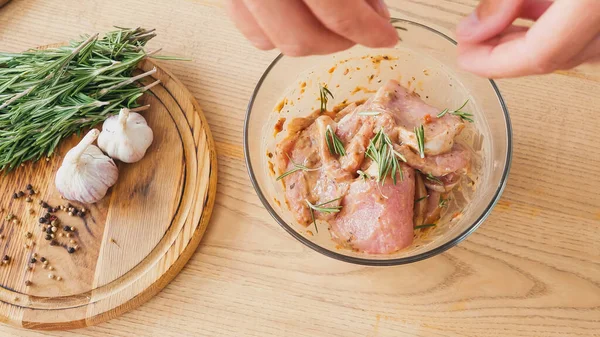 Top view of chef seasoning marinated sliced chicken with rosemary in bowl — Stock Photo