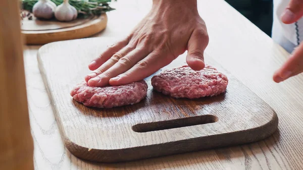 Vue recadrée du chef formant une galette hachée sur une planche à découper près des ingrédients — Photo de stock