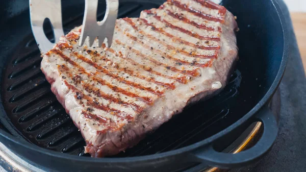 Close up of cooking tongs near beef steak on grill pan — Stock Photo