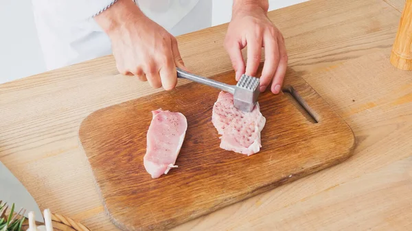 Vista cortada do chef com martelo de corte achatamento de carne de porco na mesa — Fotografia de Stock