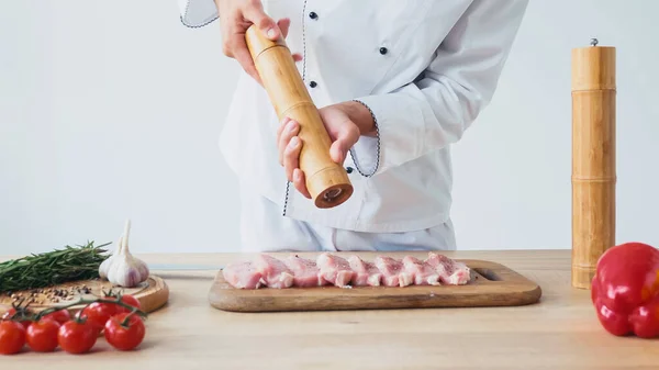 Обрезанный вид шеф-повара с соляной мельницей, приправляющий куски свиной вырезки на белом — стоковое фото