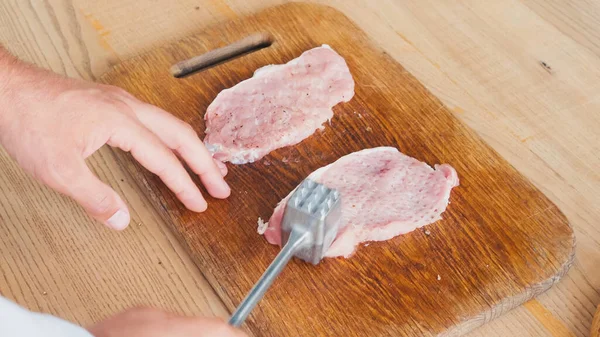 Vista parcial del chef con martillo de picado aplanando carne de cerdo en la mesa - foto de stock