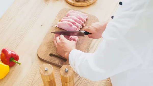High angle view of chef cutting beef tenderloin on chopping board near bell peppers — Stock Photo