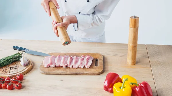 Vista parcial do chef com moinho de sal tempero pedaços de lombo de carne em branco — Fotografia de Stock