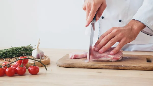 Частичный вид человека, нарезающего говяжью вырезку на доске возле помидоров черри на белом — стоковое фото