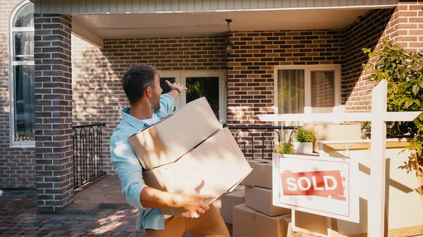 Aufgeregter Mann hält Kisten in der Hand und zeigt mit der Hand auf neues Haus — Stockfoto