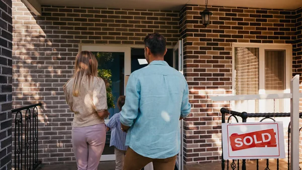 Rückansicht Familie betritt neues Haus in der Nähe der Tafel mit verkauftem Schriftzug — Stockfoto