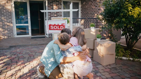 Loving family hugging near board with sold lettering and new house — Stock Photo