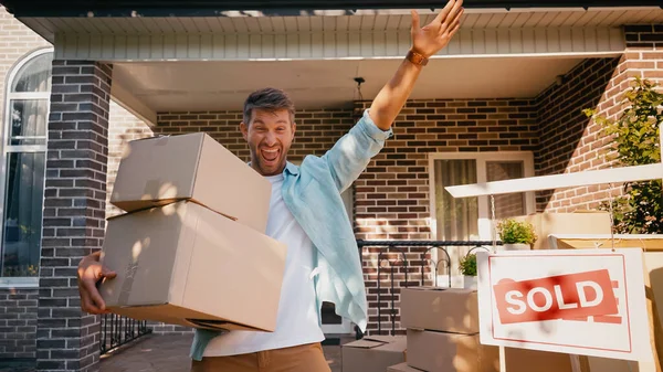 Homem surpreso segurando caixas de papelão e apontando com a mão perto da casa — Fotografia de Stock
