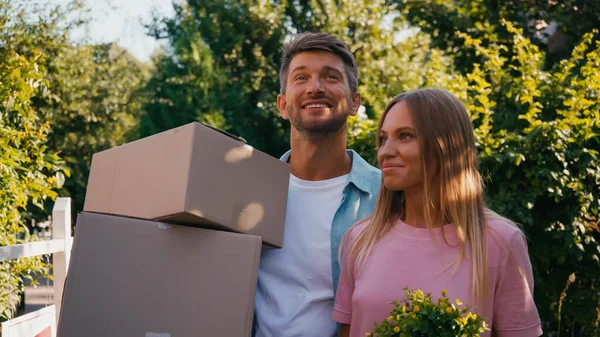 Cheerful husband and wife walking with carton boxes and plant, relocation concept — Stock Photo