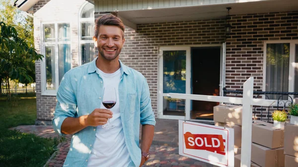 Uomo gioioso che tiene un bicchiere di vino rosso vicino alla nuova casa — Foto stock