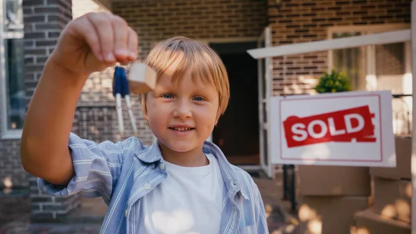 Freudiger Junge blickt in Kamera und hält Schlüssel in der Nähe des neuen Hauses — Stockfoto