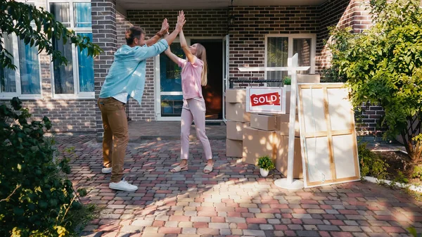 Alegre pareja dando alta cinco cerca de casa nueva y vendido tablero - foto de stock