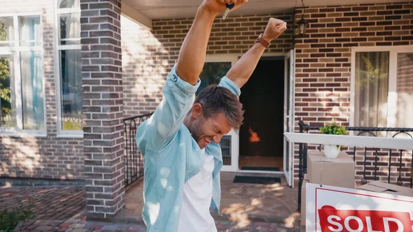 Homme excité avec les mains levées près de bord avec lettrage vendu et nouvelle maison — Photo de stock