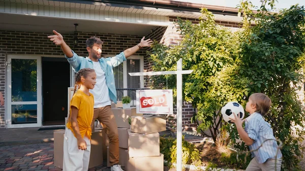Glücklicher Junge hält Fußball in der Nähe von Vater und Schwester in neuem Haus — Stockfoto
