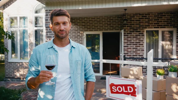 Jubelnder Mann hält Glas Rotwein in der Nähe des neuen Hauses — Stockfoto