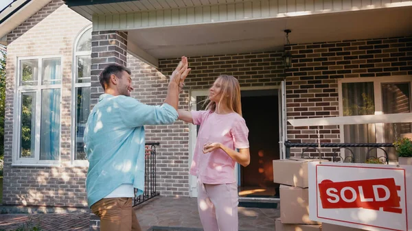 Glückliches Paar gibt High Five in der Nähe von neuem Haus und verkaufte Vorstand — Stockfoto