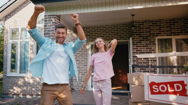 Homme excité se réjouissant près de la femme, nouvelle maison et planche vendue — Photo de stock