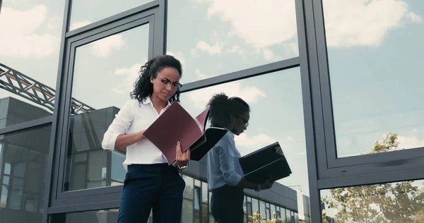 Busy african american businesswoman with folders standing near building on urban street — Stock Photo