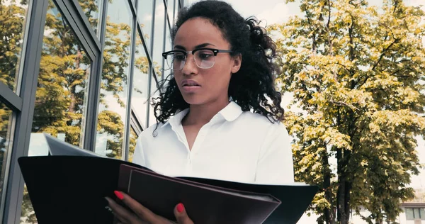 Afrikanisch-amerikanische Geschäftsfrau sucht Ordner in der Nähe von Gebäude außerhalb — Stockfoto