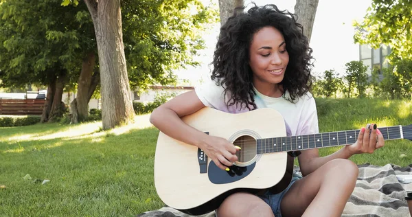Feliz mulher afro-americana tocando guitarra acústica no parque — Fotografia de Stock