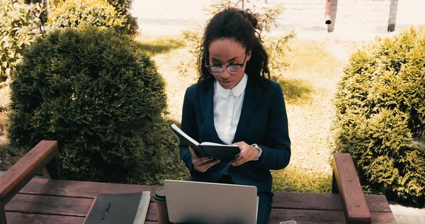 Femme d'affaires afro-américaine avec ordinateur portable et ordinateur portable assis sur le banc — Photo de stock