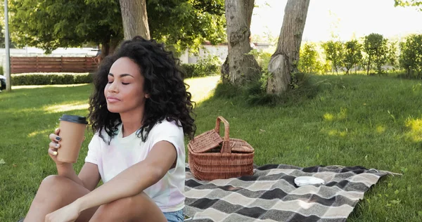 Giovane donna afroamericana che tiene il caffè da fare durante il picnic nel parco — Foto stock