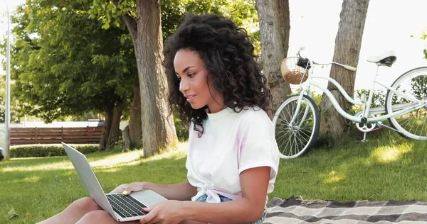 Freelancer americano africano encaracolado olhando para laptop no parque — Fotografia de Stock