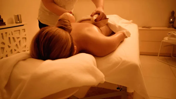 Masajista profesional masajeando a mujer joven con conchas de mar en el salón de spa - foto de stock