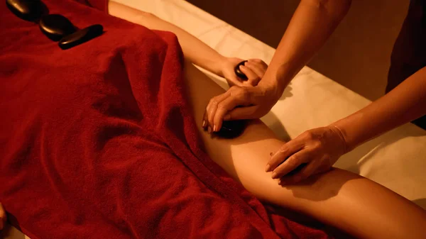 Обрезанный вид профессионального массажиста, делающего массаж горячими камнями для клиента — стоковое фото