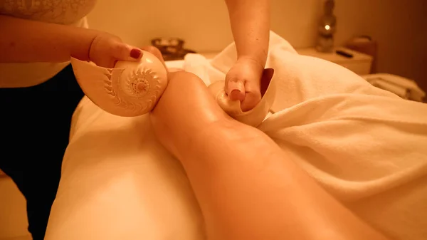 Cropped view of therapist massaging leg of young client with sea shells in wellness center — Stock Photo