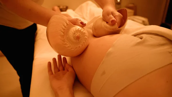 Partial view of therapist massaging leg of young woman with sea shells in wellness center — Stock Photo