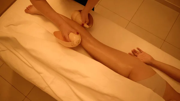 Top view of therapist massaging leg of young client with sea shells in wellness center — Stock Photo