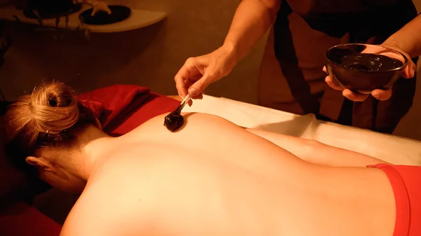 Therapist applying mud with spatula on body of young client in spa salon — Stock Photo