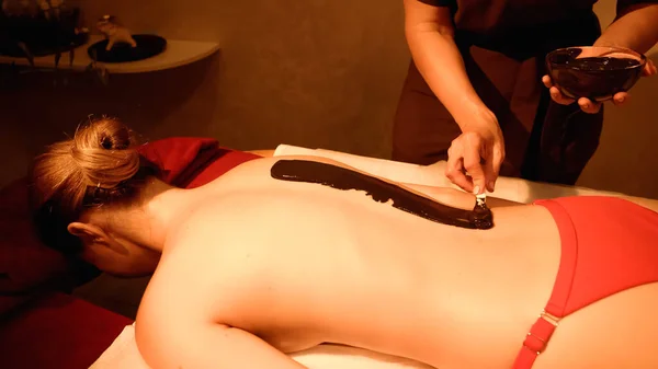 Masseur application de boue avec spatule sur le corps du jeune client dans le salon de spa — Photo de stock