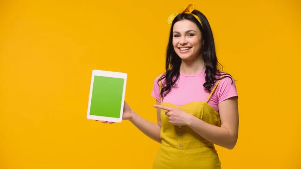 Femme souriante pointant vers tablette numérique avec écran vert isolé sur jaune — Photo de stock