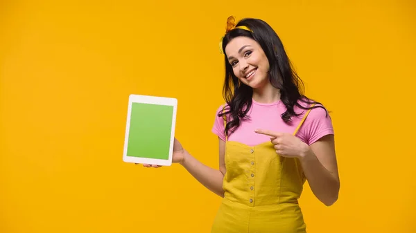 Mulher morena apontando para tablet digital com tela verde isolada no amarelo — Fotografia de Stock