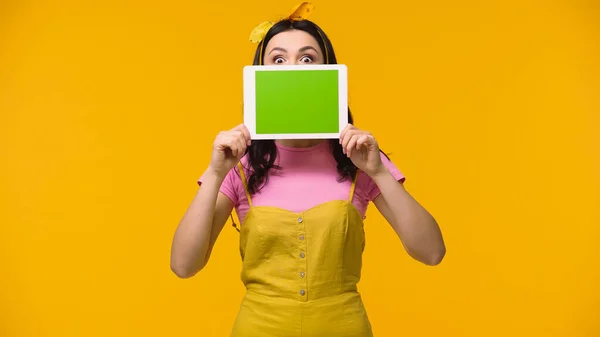 Amazed woman covering face with digital tablet isolated on yellow — Stock Photo