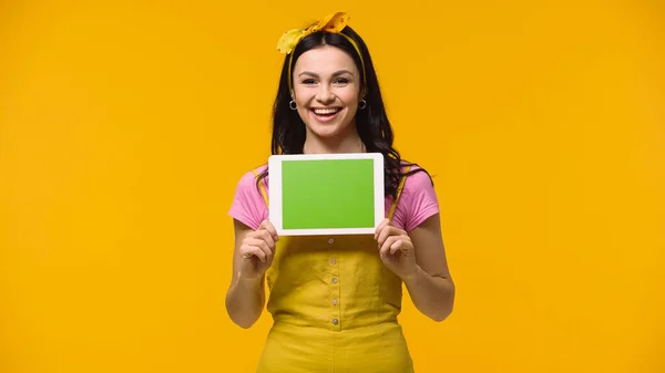 Mujer positiva sosteniendo tableta digital con pantalla verde aislada en amarillo - foto de stock