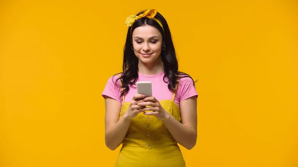 Mujer bonita joven usando teléfono inteligente y sonriendo aislado en amarillo - foto de stock