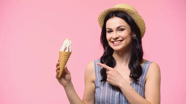Brunette woman in sun hat pointing at ice cream isolated on pink — Stock Photo