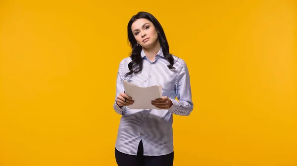 Brunette businesswoman holding papers while looking at camera isolated on yellow — Stock Photo