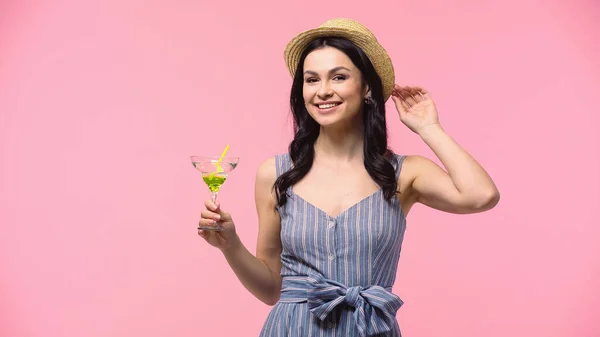 Улыбающаяся женщина в солнечной шляпе держит коктейль изолирован на розовый — стоковое фото
