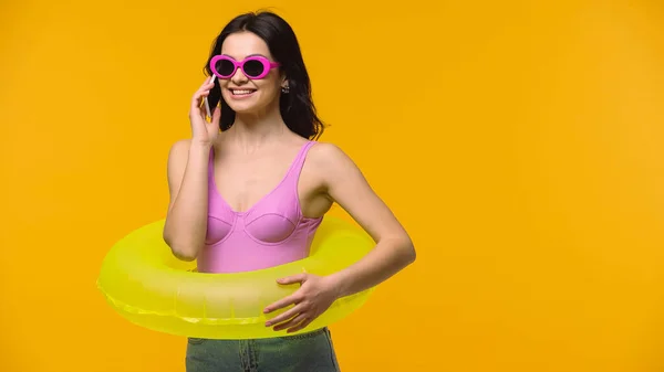 Mujer sonriente en gafas de sol y anillo de natación hablando en smartphone aislado en amarillo - foto de stock